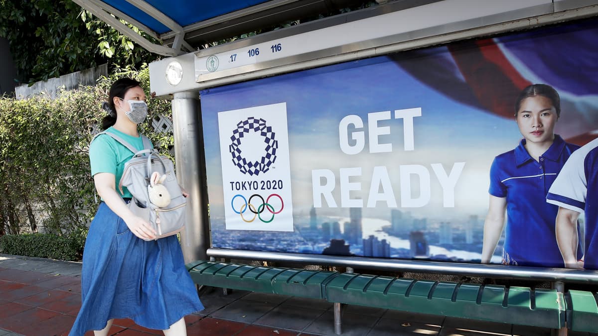 Nainen kävelee bussipysäkillä olevan Tokion olympialaisten mainoksen ohi Bangkokissa.