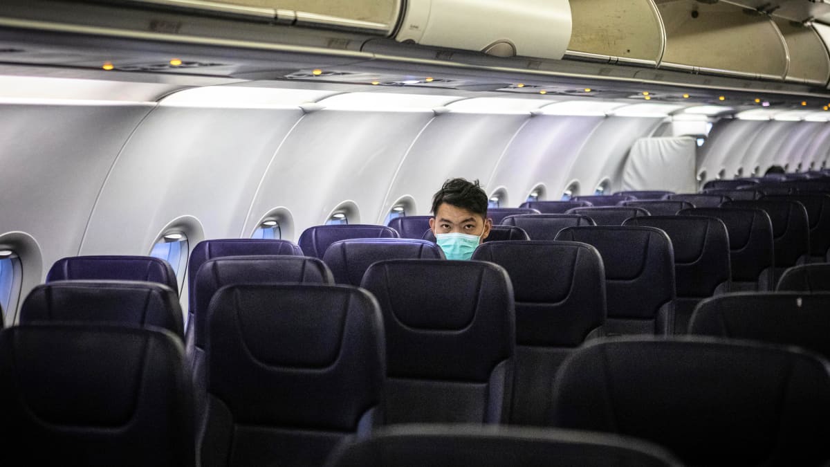 Hengityssuojaimeen pukeutunut matkustaja istuu tyhjässä lentokoneen matkustamossa.
