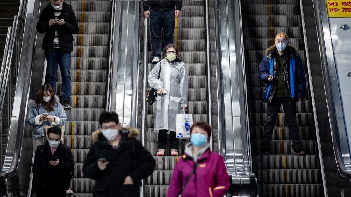 Hengityssuojiin pukeutuneita matkustajia metron rullaportaissa Shanghaissa.