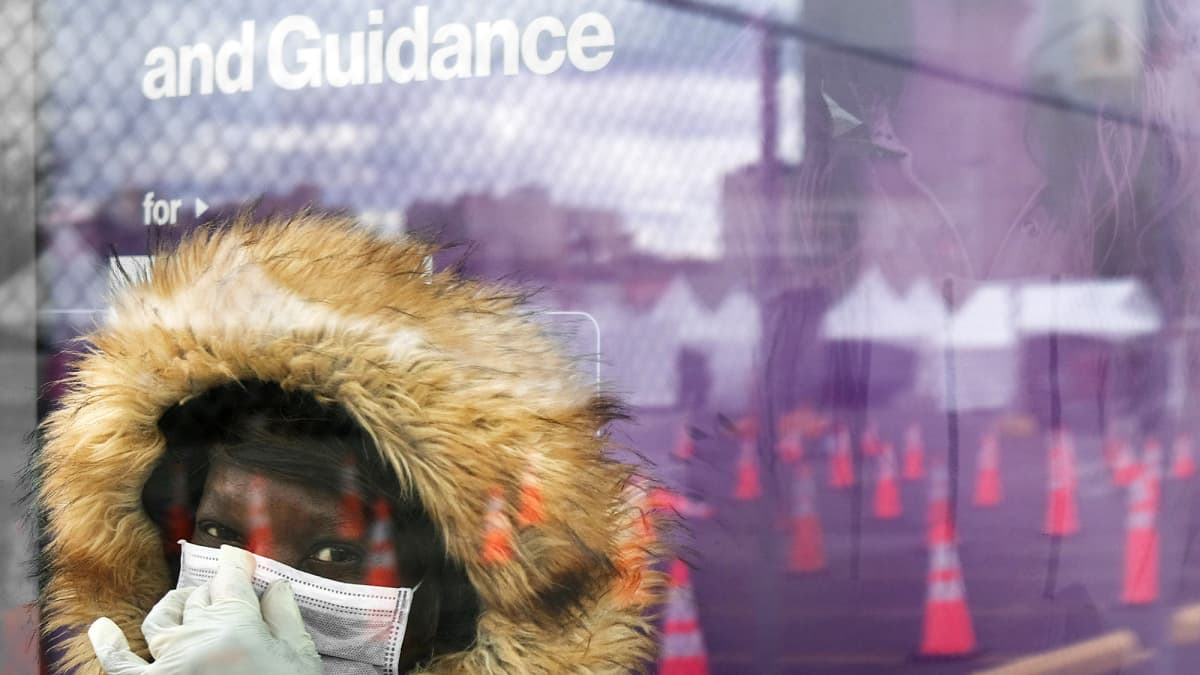 Hengityssuojaimeen pukeutunut nainen odottaa linja-autoa bussipysäkillä New Yorkissa.