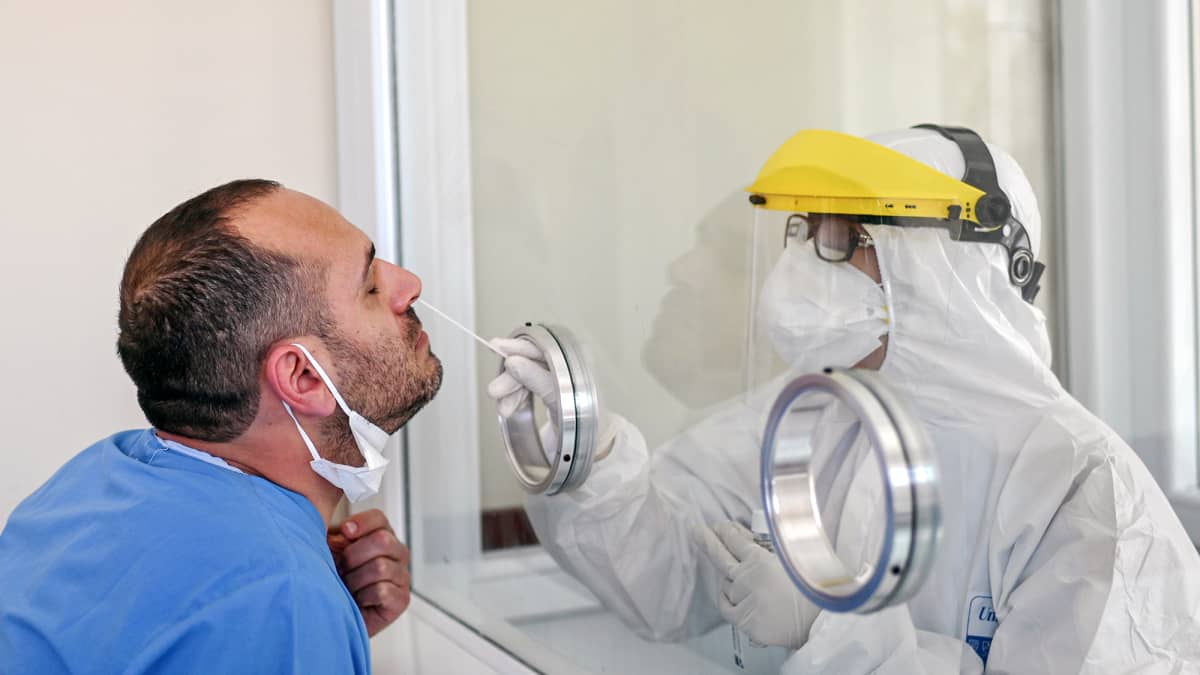 Suojavarusteisiin pukeutunut terveydenhuollon työntekijä ottaa koronavirustestiä nenästä.