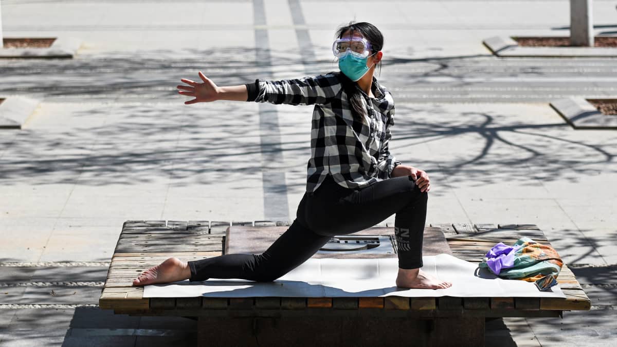 Hengityssuojaimeen ja suojalaseihin pukeutunut nainen venyttelee Pekingissä