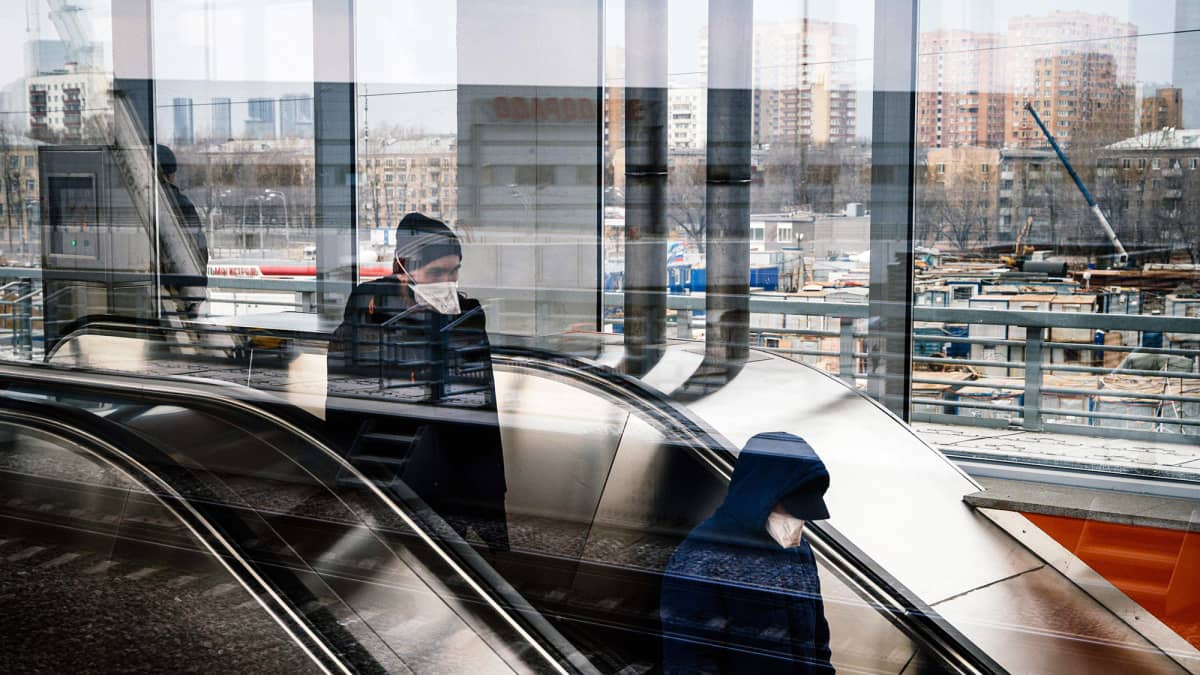 Hengityssuojaimiin pukeutuneita matkustajia Moskovan metron rullaportaissa.