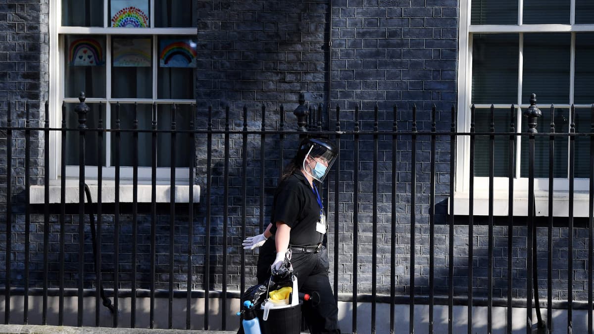 Suojavarustukseen pukeutunut siistijä poistuu pääministerin asunnolta Lontoossa.