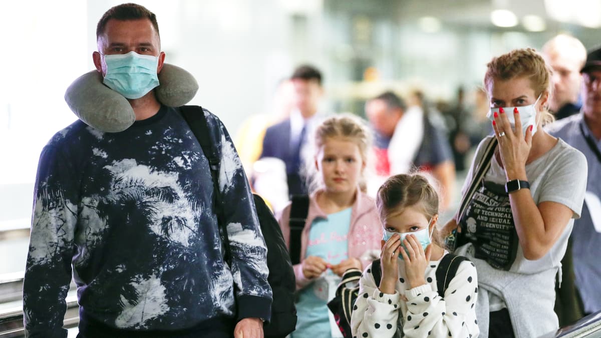 Hengityssuojaimiin pukeutunut perhe Suvarnabhumin lentoasemalla Thaimaassa.