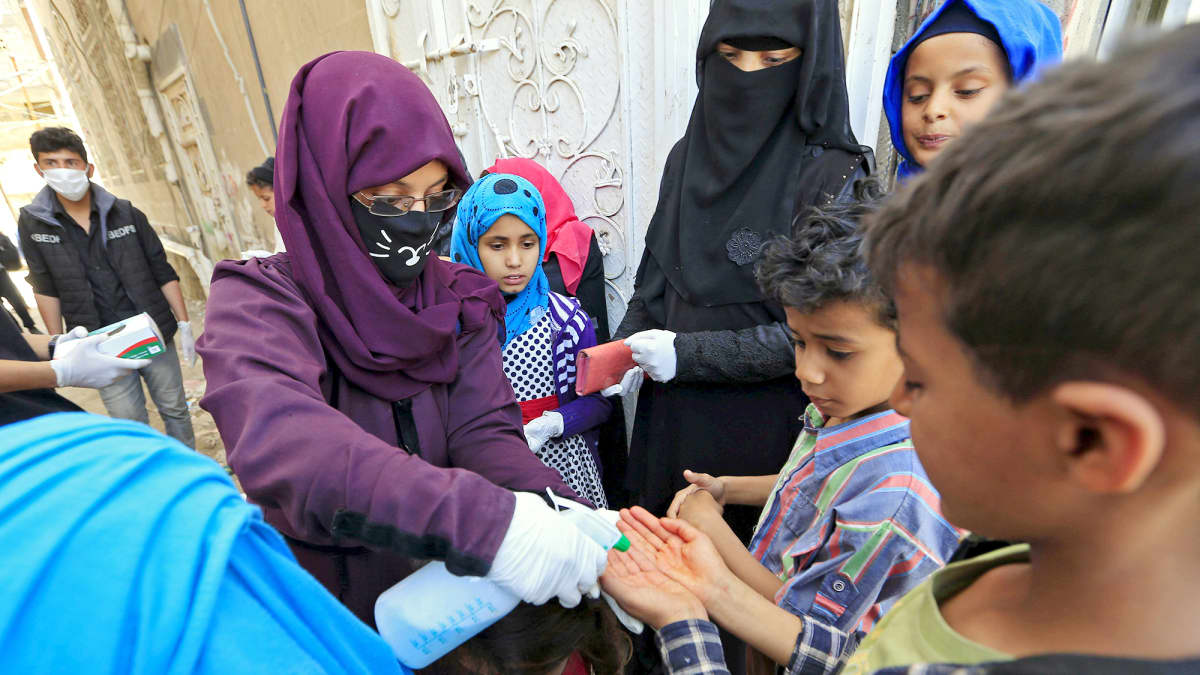 Vapaaehtoistyöntekijä desinfioi lasten käsiä kadulla Sanaassa.