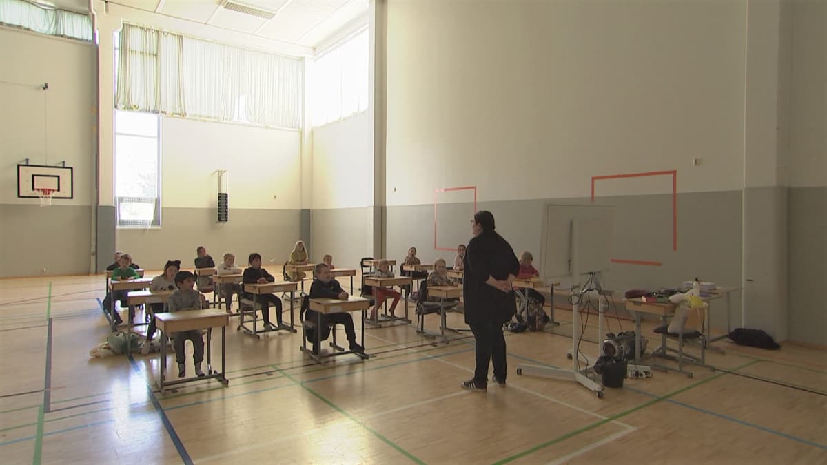 Oppilaat istuvat väljästi pulpettiensa takana liikuntasaliin järjestetyssä luokassa Peltosaaren koululla Riihimäellä.