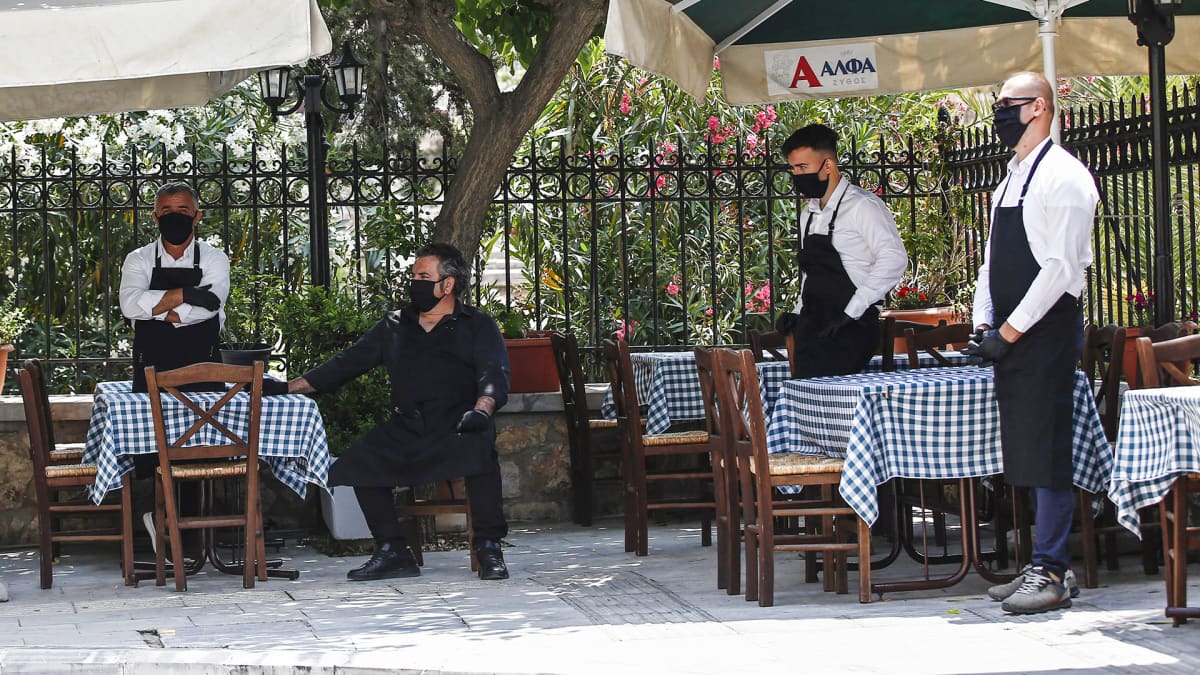 Ateenassa kasvomaskeihin suojautuneet tarjoilijat odottavat asiakkaita.