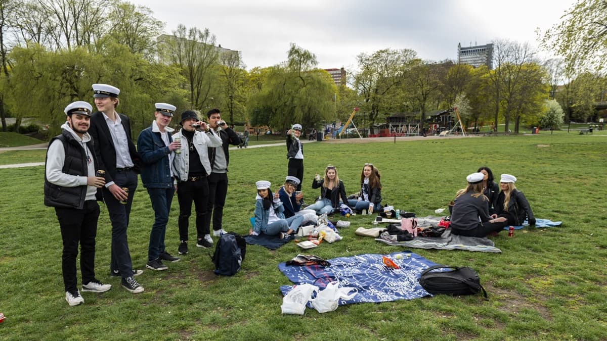 Ylioppilaslakkisia nuoria picnicillä puistossa. 