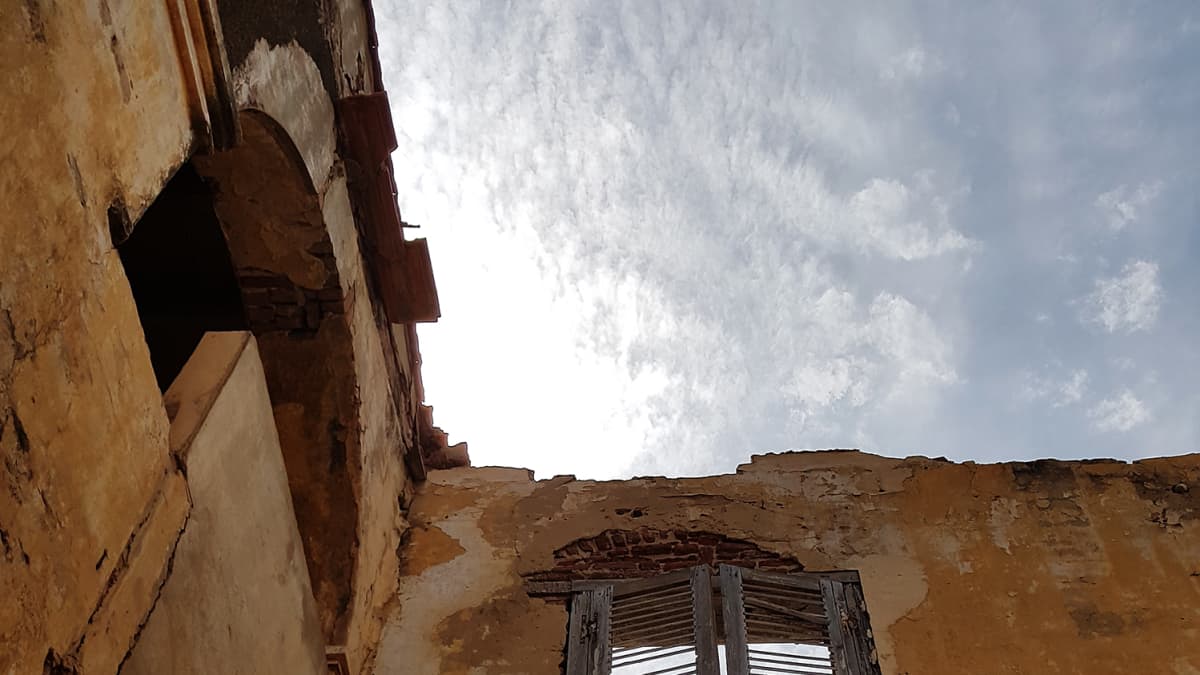 Kuvassa on talon seinä ja toisen kerroksen puinen ovi, jonka takana näkyy taivas.