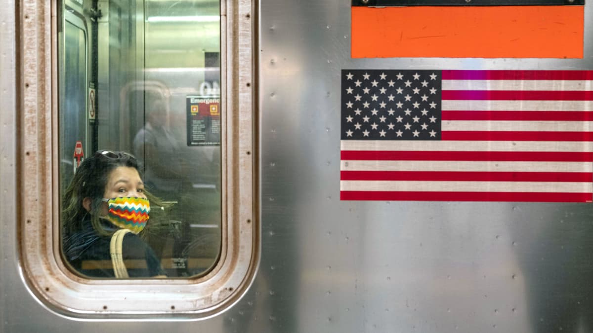 Kasvomaskiin pukeutunut matkustaja New Yorkin metrossa 
