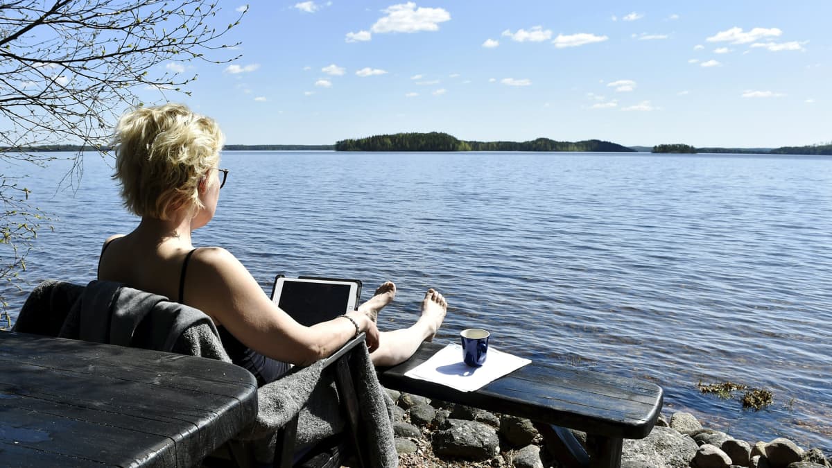 Kuvassa nainen tekee etätöitä järven rannalla.