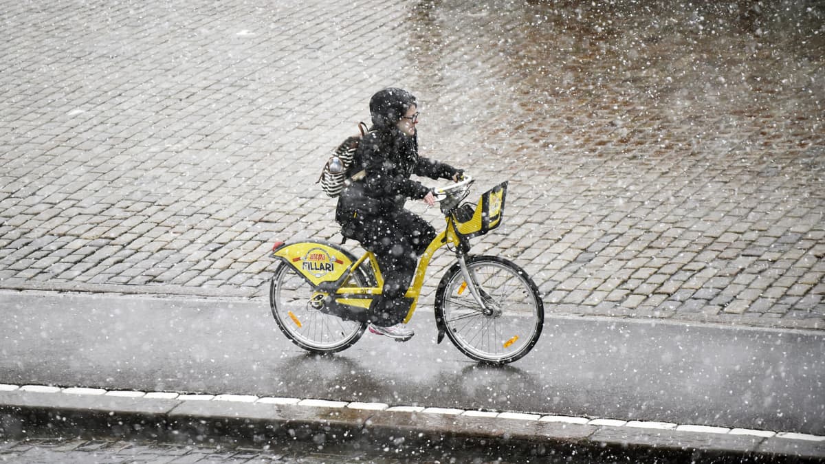 Nainen pyöräilee kaupunkipyörällä lumisateessa Helsingissä.