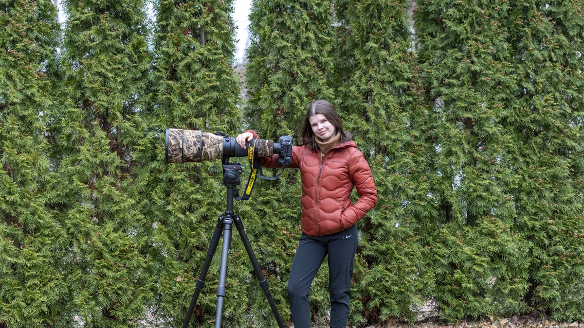 Nuori nainen ison kameran kanssa luonnossa.