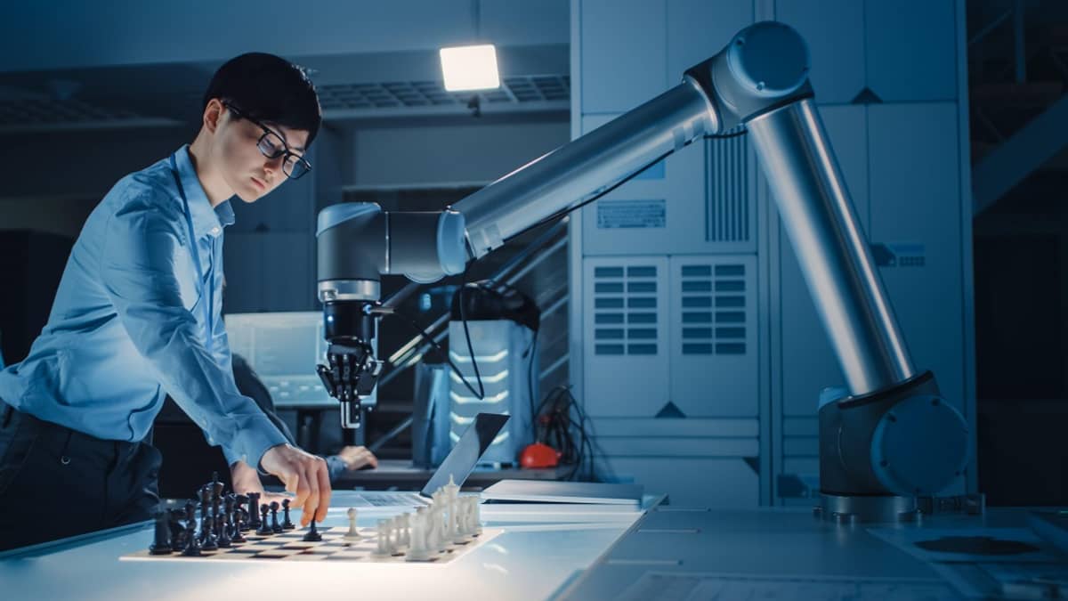 Nuori japanilaismies tekee ensimmäistä siirtoaan šakkilaudalla. Vastapäätä robottivarsi, joka on jo avannut pelin valkoisilla nappuloillaan. 