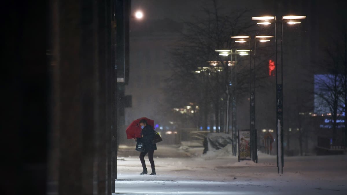Sateenvarjolla varustautunut jalankulkija lumisateessa Helsingissä.