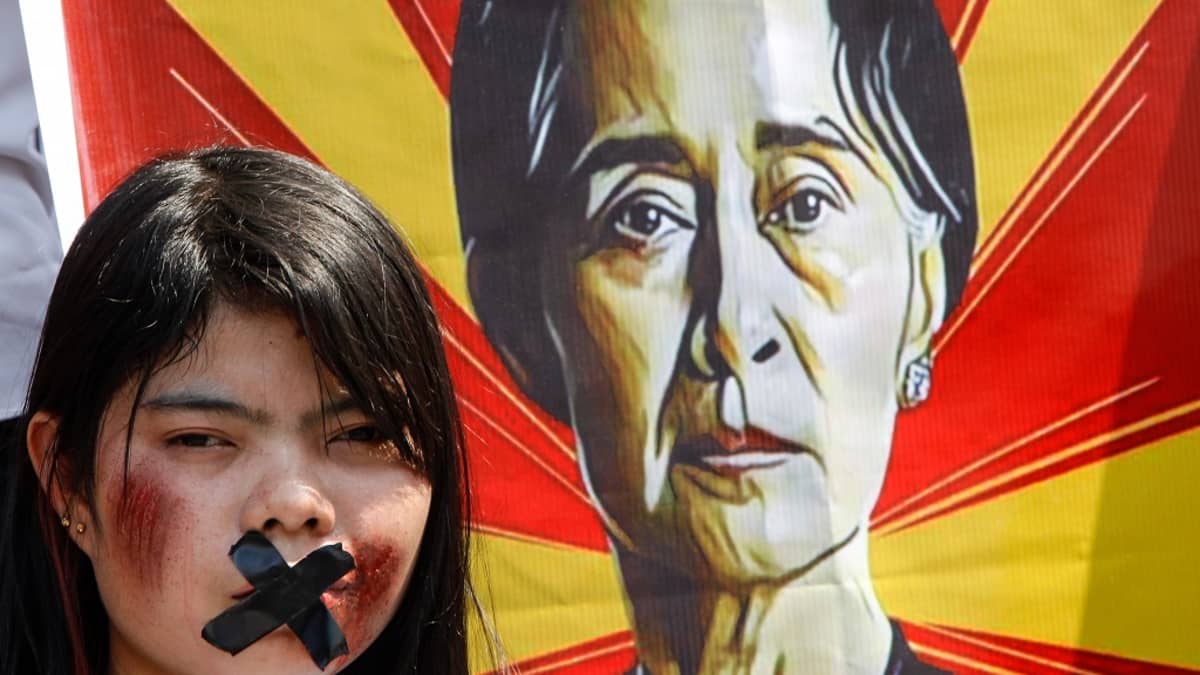 Suu Kyin kannattaja on teipannut suunsa kiinni, taustalla Suu Kyin kuva bannerissa.