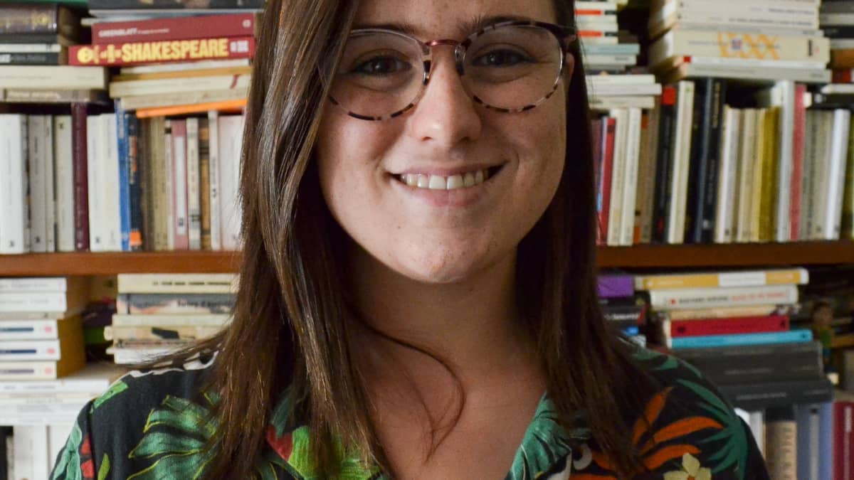 Espanjalainen Lucia Sanz Astier tulee Suomeen kesällä varhaiskasvatuksen opettajaksi. Kuvassa hän hymyilee kirjahyllyn edessä.