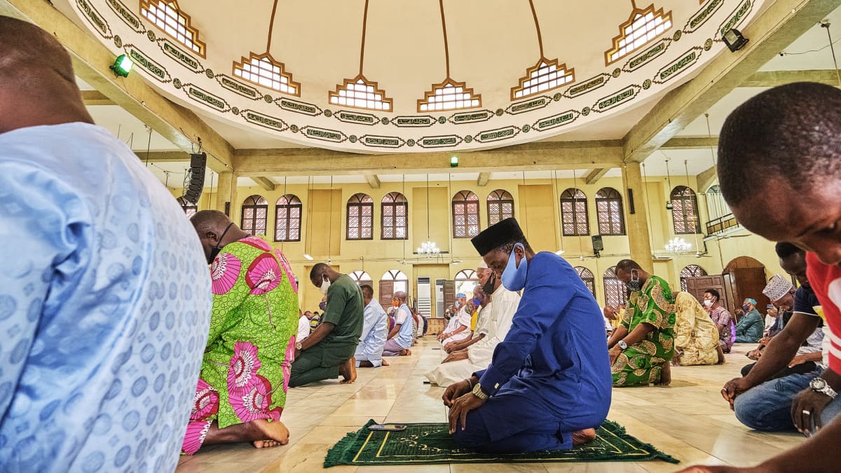 Nigerialaisia ihmisiä hengityssuojaimet kasvoilla rukoilemassa moskeijassa.