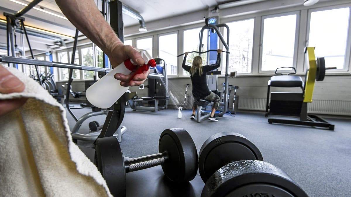 Treenaaja suihkuttaa desinfiointiainetta painoihin kuntosalilla.