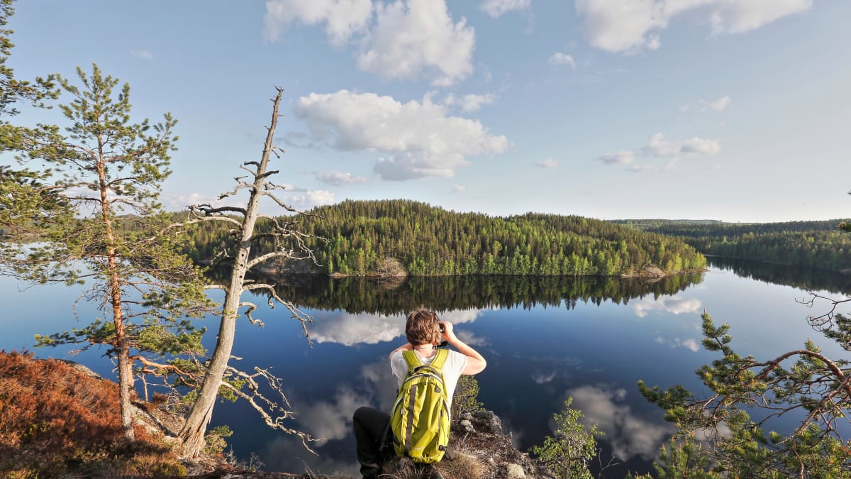 retkeilijä katsoo järvimaisemaa korkealta kalliolta
