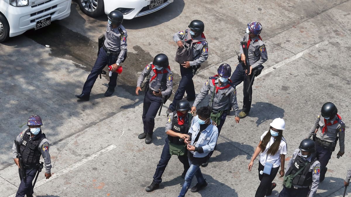 Poliisit taluttavat pidätettyä mielenosoittajaa kadulla.