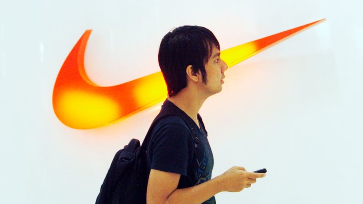 Indonesialainen mies kävelee Niken valaistun logon ohi kauppakeskuksessa.