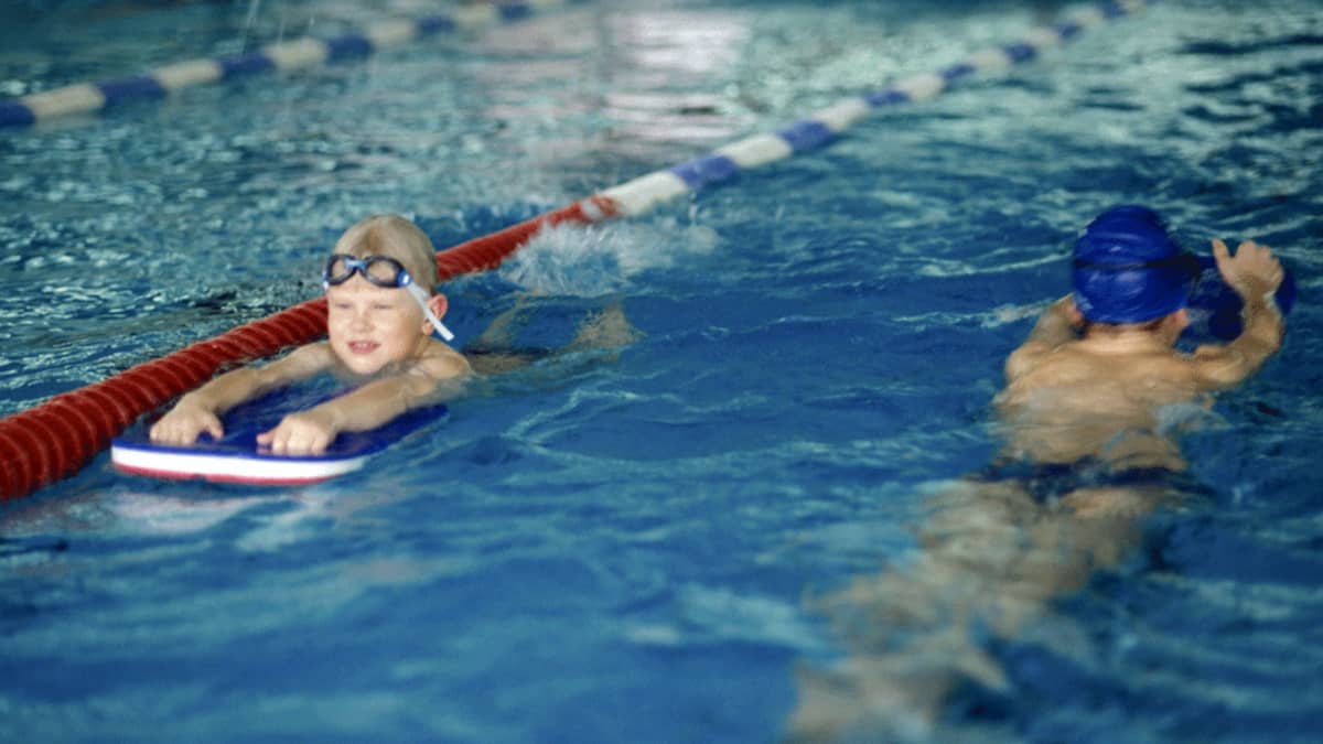 Kaksi lasta harjoittelee uintiliikkeitä uintilaudan avulla.