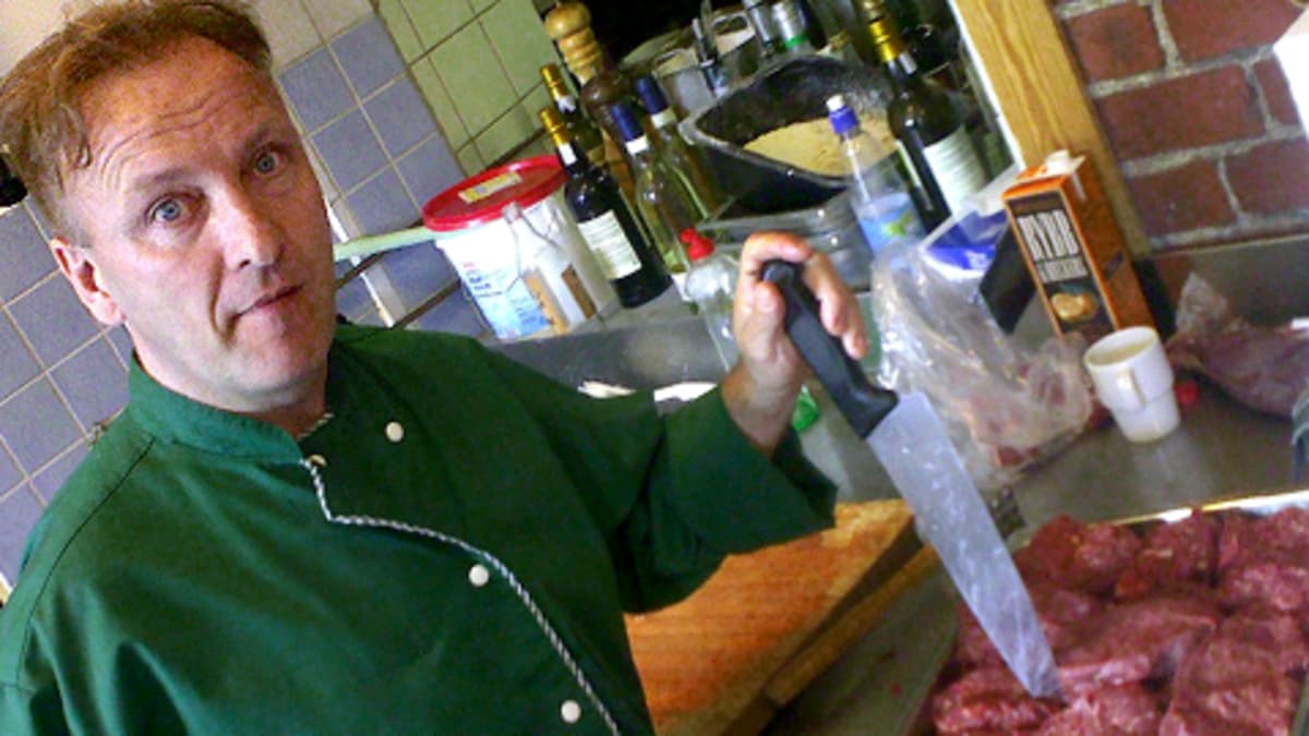 Mieskokki keittiössä lihapalojen äärellä, veitsi kädessään