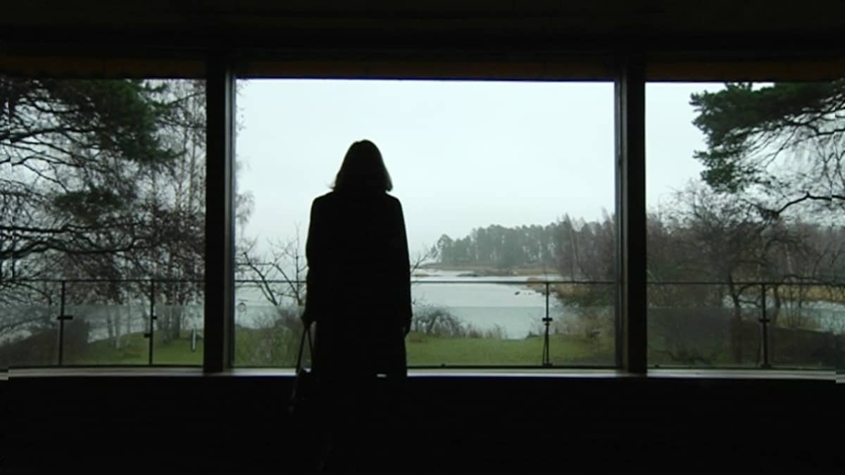 Nainen katsoo ikkunasta avautuvaa merimaisemaa.