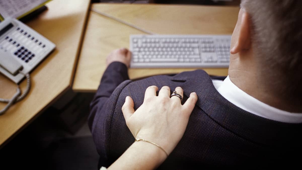 naisen käsi koskettaa työpöydän ääressä istuvaa miestä olkapäähän