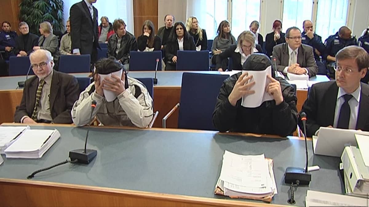 Kaksi syytetyistä paperit kasvoilla oikeuden pöydän ääressä.
