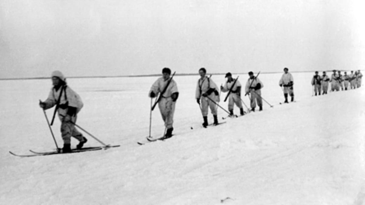 Lumipukuiset sotilaat hiihtävät järven jäällä talvisodassa.
