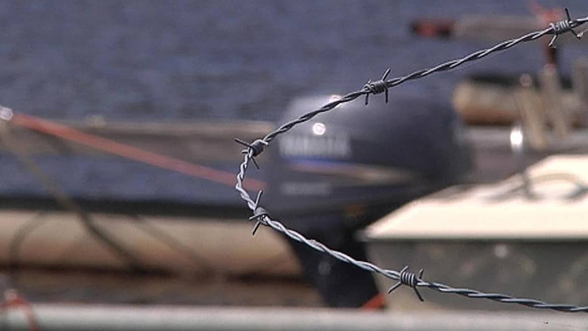 Perämoottori piikkilangalla suojatun portin takana.
