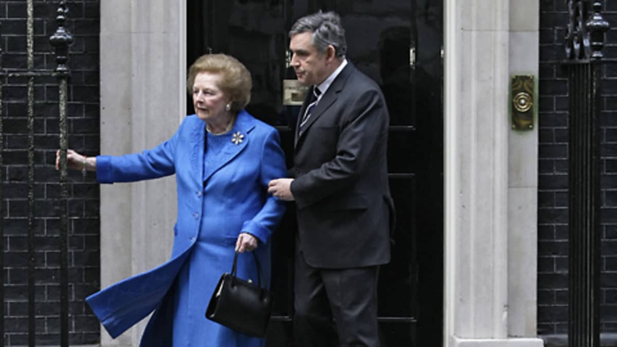 Gordon Brown pitää kiinni Margaret Thatcheristä, joka pitää toisella kädellään kiinni rautaportista.