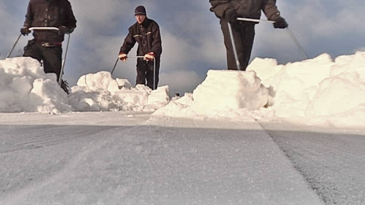 Kolme miestä kolaamassa katolta lunta pois.