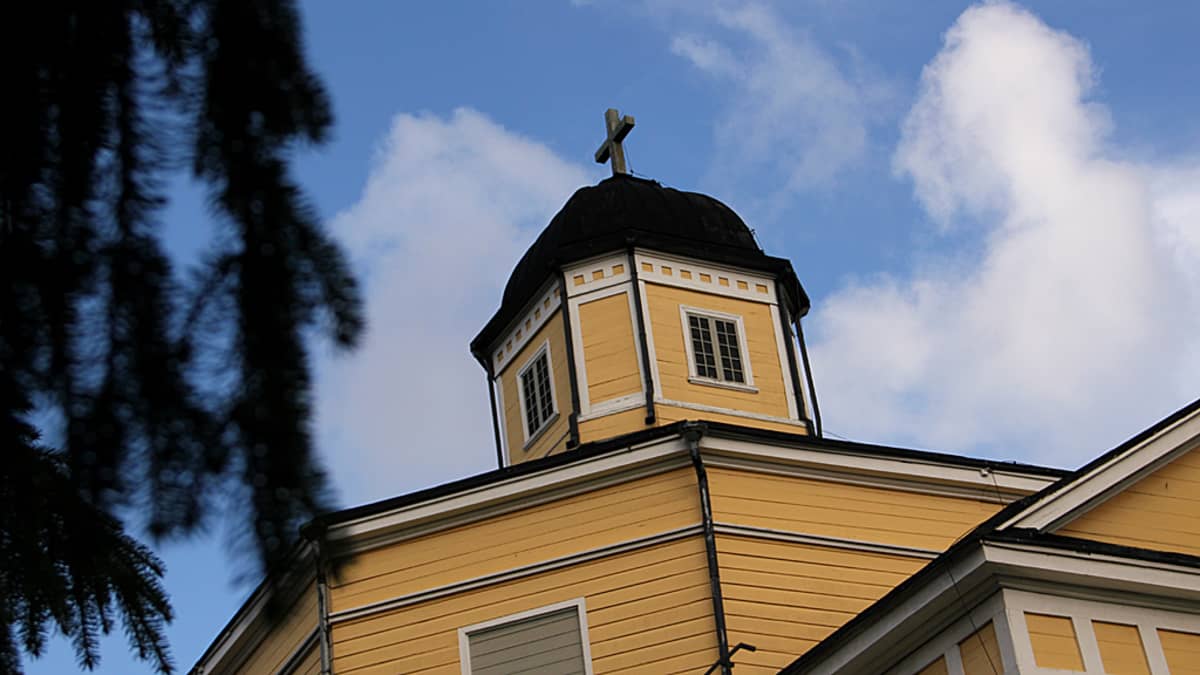 Kuvassa Juuan puukirkon torni. Etualalla näkyy kirkon pihalla kasvavan kuusen oksaa. 