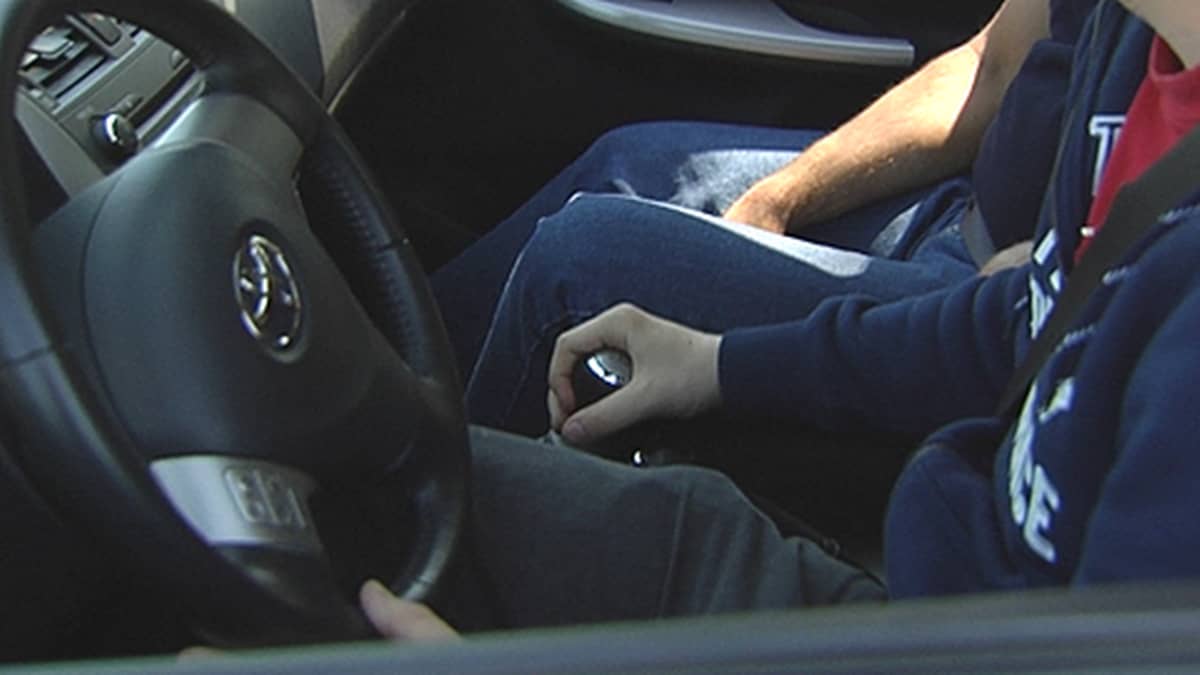 Nuori mies istuu kujettajan paikalla autossa kätensä vaihdekepillä.