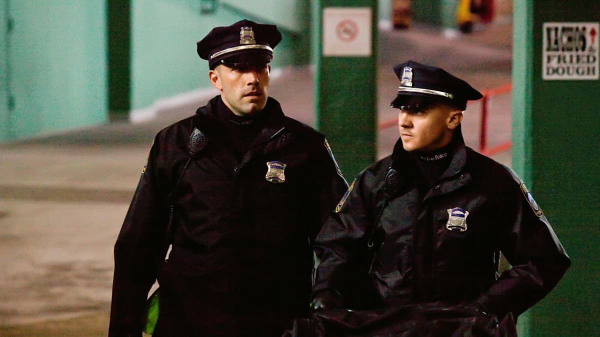 Kaksi poliisiunivormuihin sonnustautunutta miestä kävelee vihreäseinäisessä parkkihallissa.