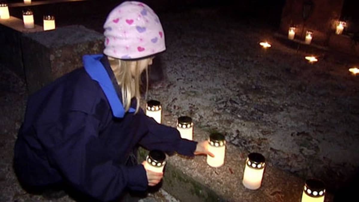 A girl sets a candle by a grave.