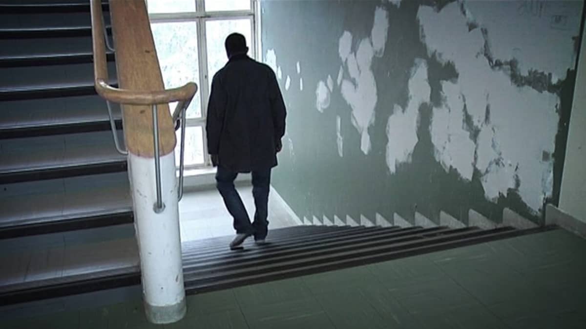 Mies kävelee portaita alas ränsistyneessä rappukäytävässä.