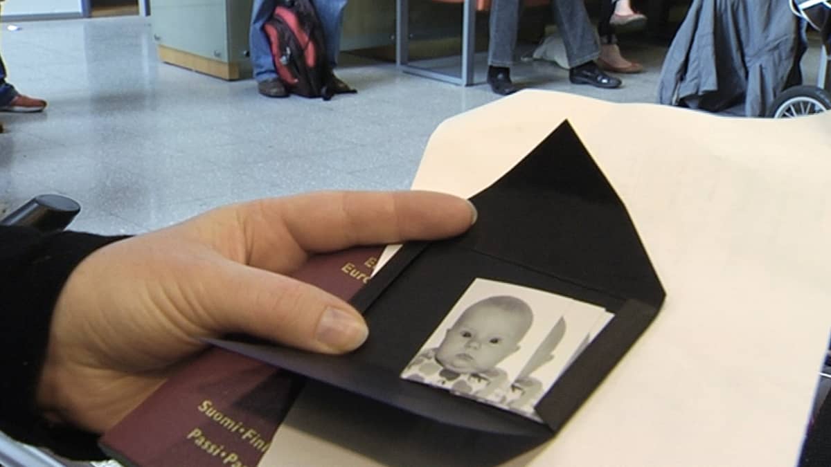 Henkilö pitelemässä vauvasta otettuja passikuvia sekä passia.