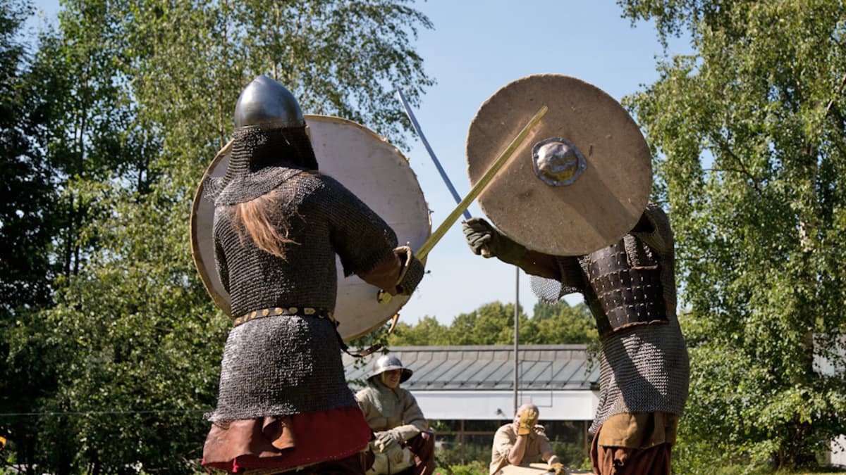 Keskiaikaisiin taisteluasuihin pukeutuneet harrastajat miekkailevat.