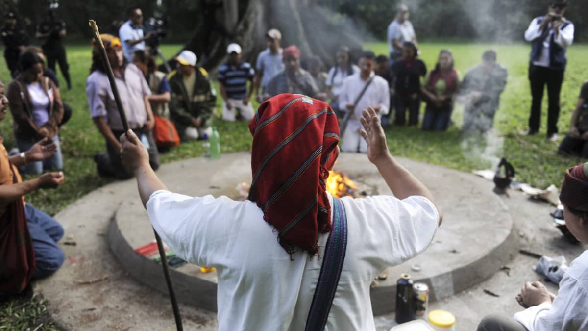 Shamaani suorittaa rituaalia tulen vieressä, ympärillä ihmisiä.