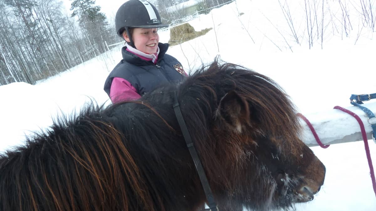 Sosiaalipedagogisen hevostoiminnan  ohjaaja Tiina Jokinen rapsuttaa islanninhevosta. 
