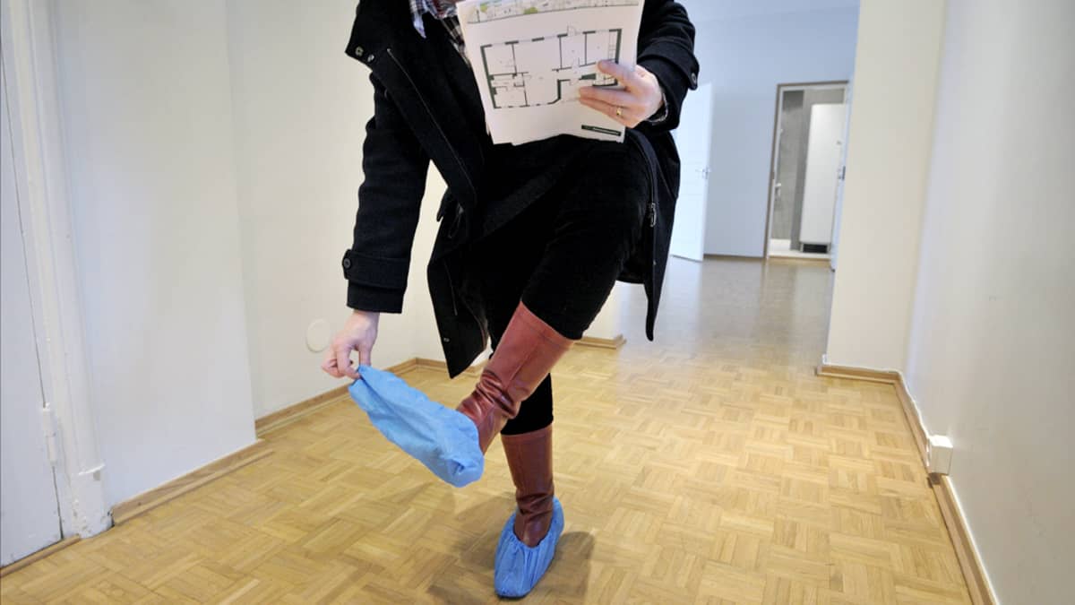Nainen riisu suojamuoveja pois kenkänsä päältä asuntonäytössä.