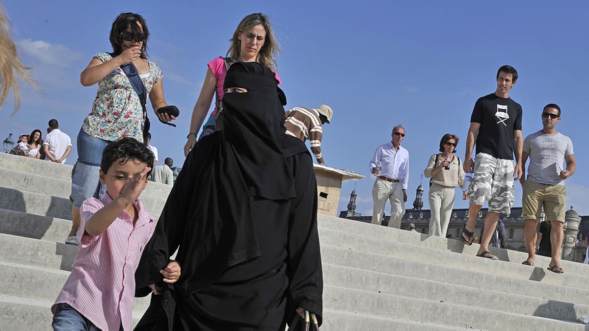 Niqabia käyttävä nainen kävelee lapsen kanssa.