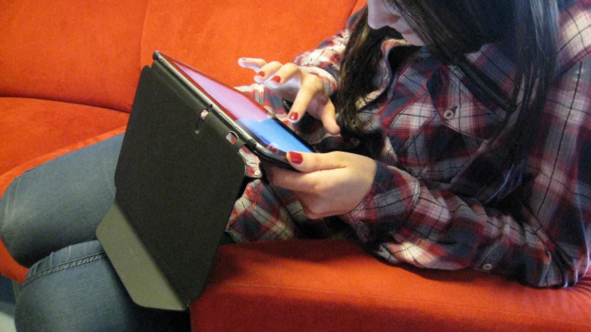 Nuori nainen selailee tablettitietokonetta sohvalla.