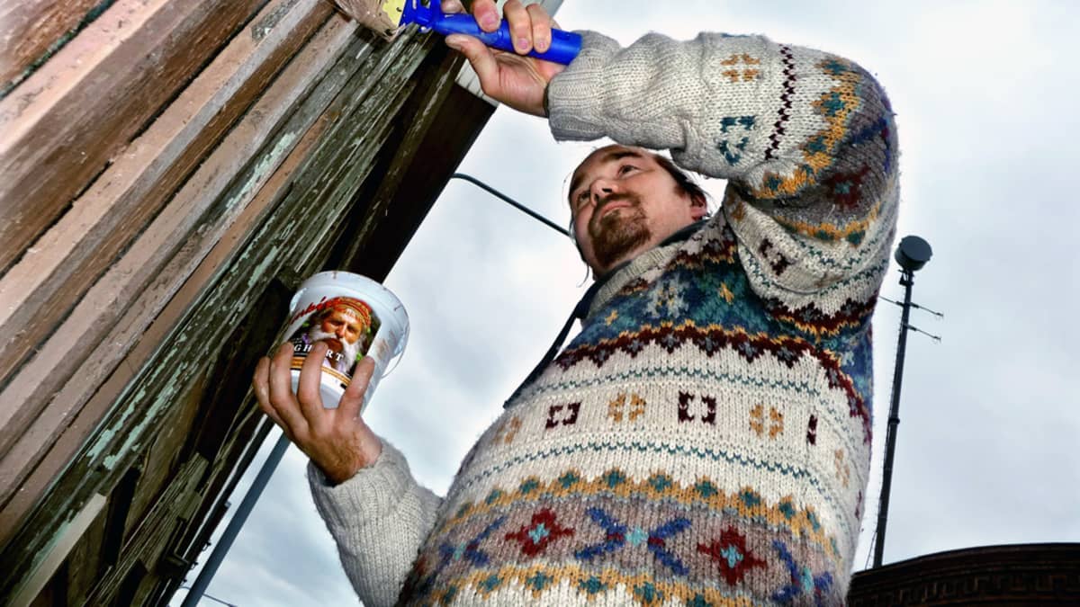 Talkoolainen maalaa puutaloa.