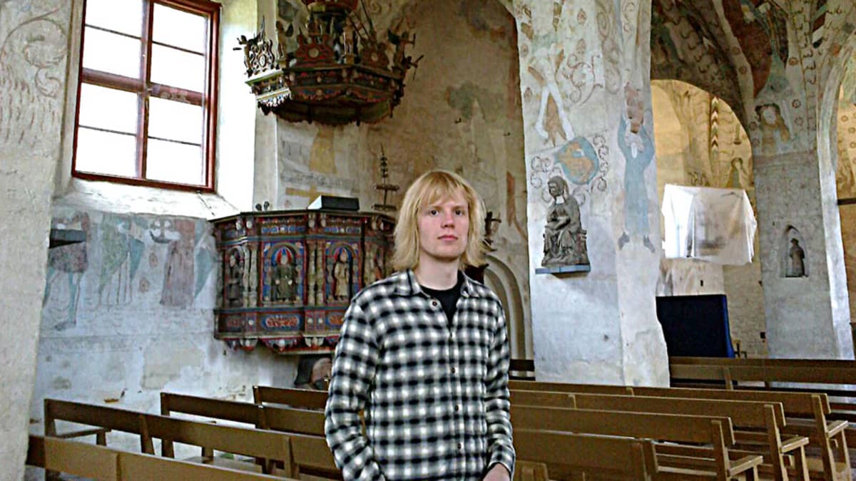 Jyrki Nissi Hattula Pyhän Ristin keskiaikaisessa kirkossa, seinillä maalauksia ja patsaita.